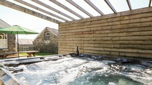 A hot tub under a wooden pergola with a stone building in the background. - The Farmhouse (Lampeter)