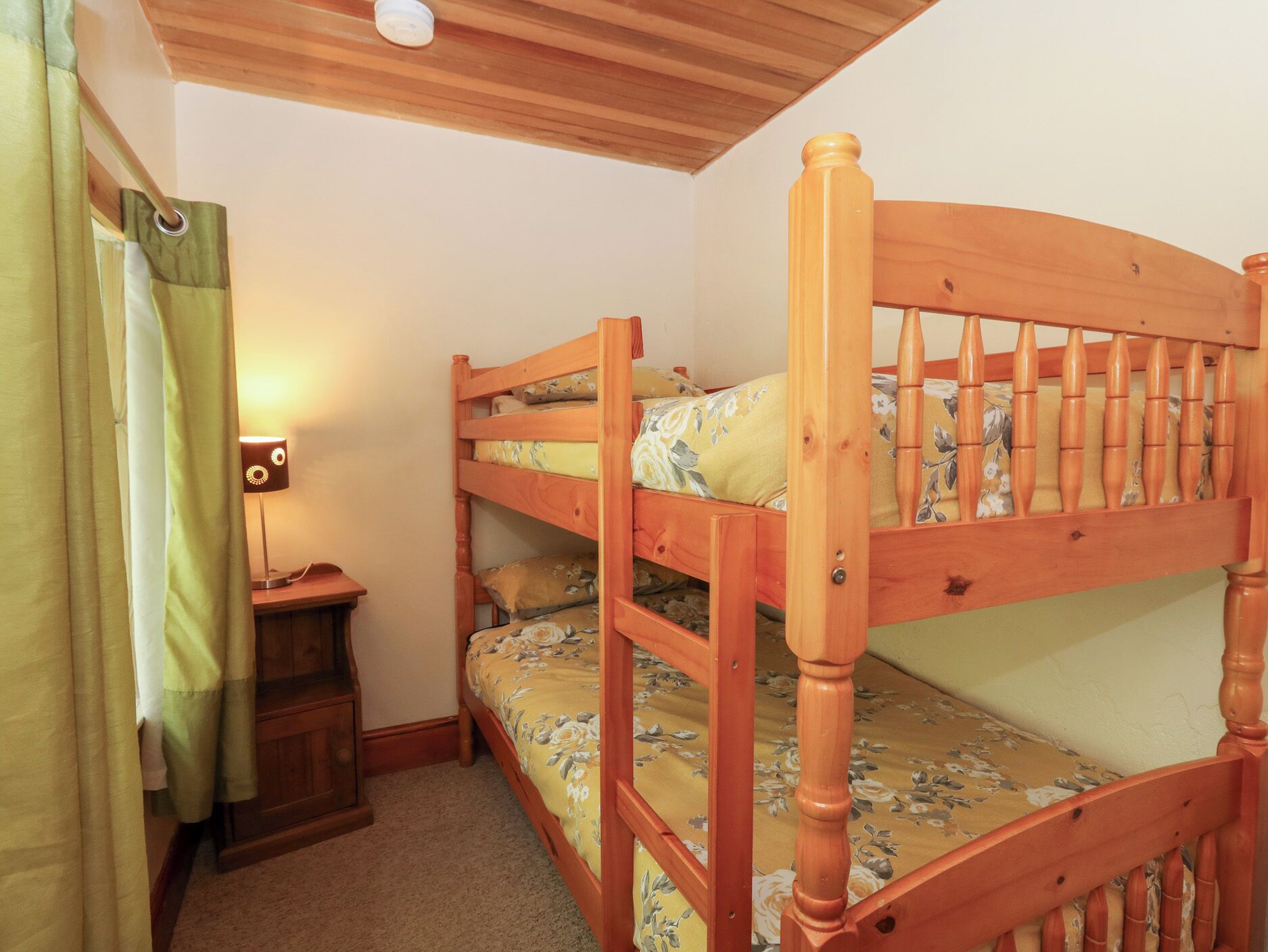 A bunk bed with floral bedding, a bedside table with a lamp, and a curtain.