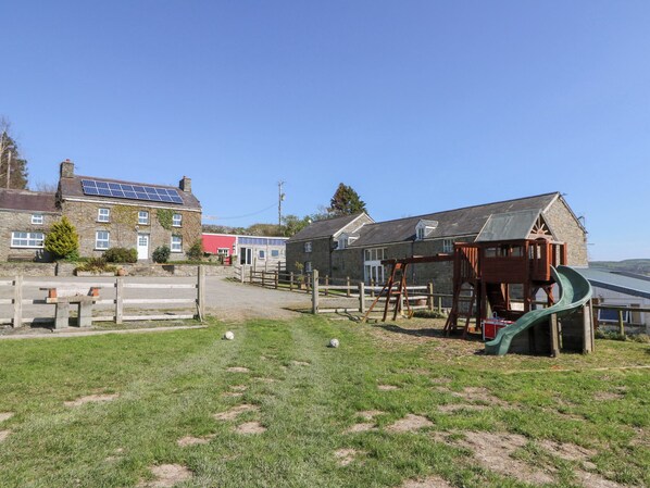 A rural setting with stone buildings, a playground, and a solar panel on a house. - The Farmhouse (Lampeter)