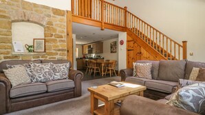 A cozy living room with two sofas, a wooden coffee table, and a stone wall. A wooden staircase leads to an upper level. - The Granary (Thirsk)