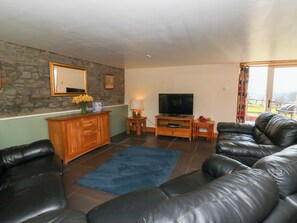 A living room with a stone wall, a wooden cabinet, a television, and leather sofas.