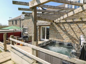 A stone building with a wooden deck, a hot tub, and outdoor seating with a green umbrella.