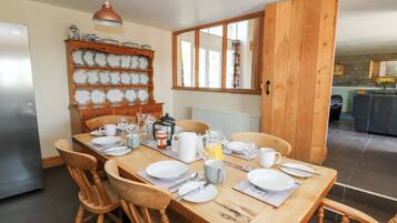Un comedor con una mesa de madera dispuesta para cuatro personas, rodeada de sillas de madera. Hay una cafetera y una jarra sobre la mesa.