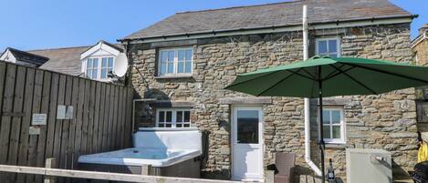 A stone house with a hot tub, a wooden fence, and a green umbrella.