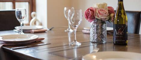 A dining table set with plates, wine glasses, a bottle of wine, and a vase with flowers.