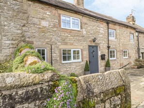A stone building with multiple windows and a door, surrounded by stone walls and greenery. - Daisy Cottage (Matlock)