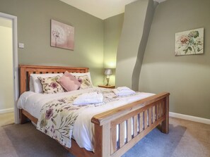 A neatly made bed with floral bedding, a wooden headboard, and a nightstand with a lamp. - Daisy Cottage (Matlock)