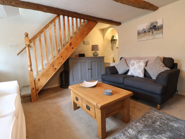 A cozy living room with a wooden staircase, a grey sofa, a wooden coffee table, and a grey patterned rug. - Daisy Cottage (Matlock)