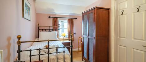 A bedroom with a metal bed frame, a wooden wardrobe, a white door with heart-shaped hooks, and a framed picture on the wall.