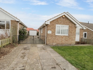 A residential property with a paved driveway leading to a gated entrance, a brick house with a white window, and a sign indicating '97 Woolsley Grove Park View'.