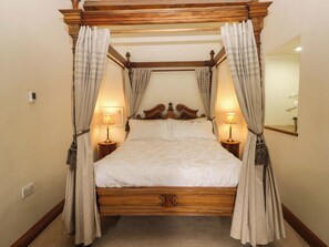 A four-poster canopy bed with curtains, bedside lamps, and a wooden headboard.