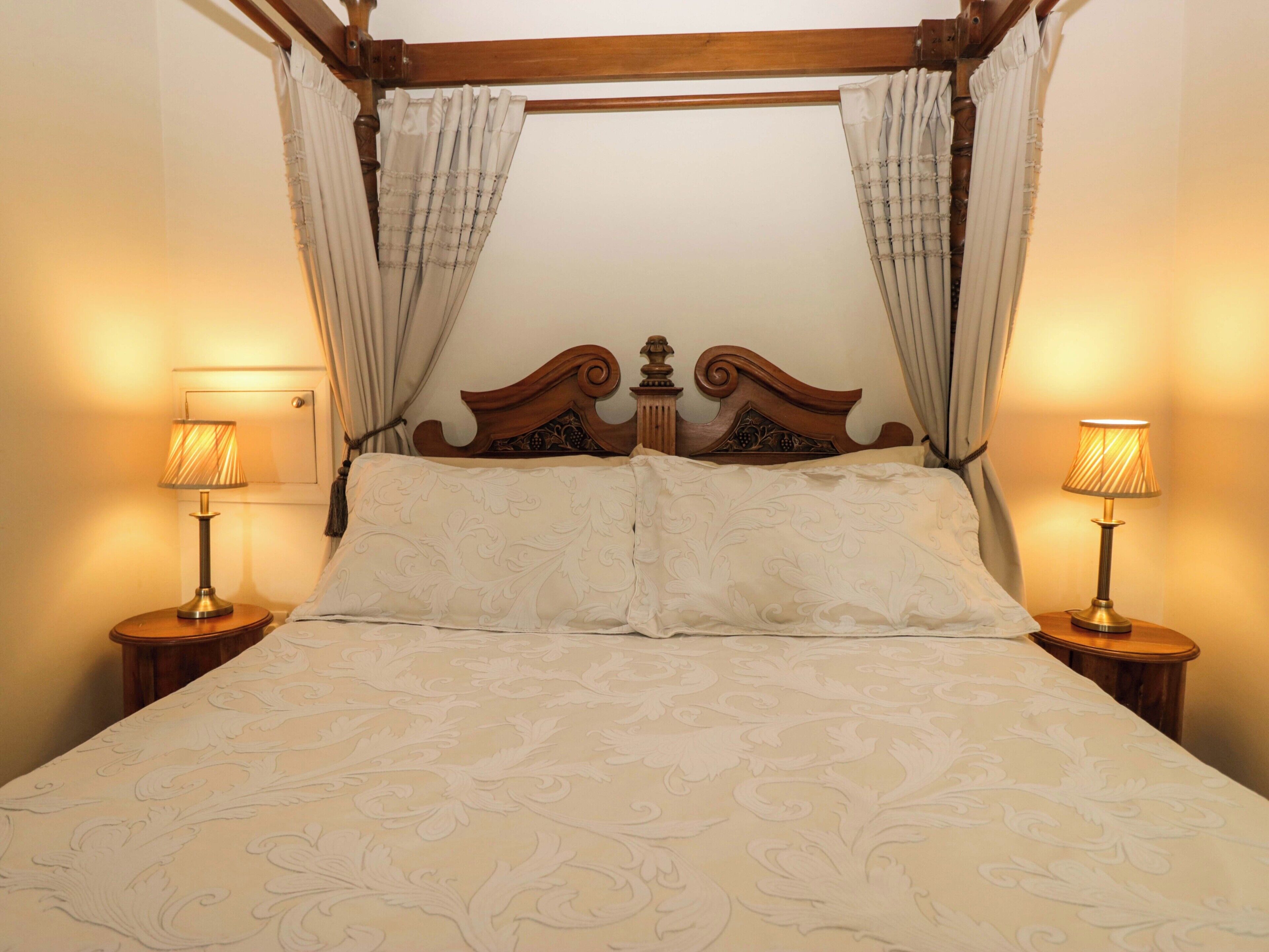 A four-poster canopy bed with a wooden headboard, two bedside lamps, and a patterned bedspread.