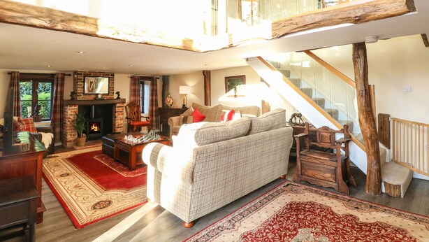 A spacious living room with a high ceiling, a fireplace, a large sofa, and a staircase leading to an upper level. - The Barn (Thetford)