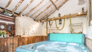 A hot tub in a rustic room with wooden beams, a clock, and a sign with hot tub rules. - The Barn (Thetford)