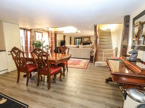 Un vaste espace de vie comprenant une table à manger en bois, des chaises à revêtement rouge, un canapé et un escalier menant à un autre niveau.
