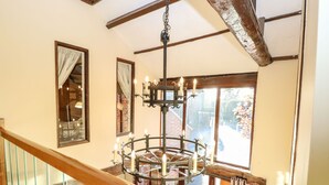 A staircase with a wooden handrail and glass balustrade, leading to a room with a chandelier, a large window with curtains, and a view of a garden. - The Barn (Thetford)