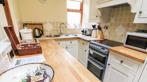 A kitchen with white cabinets, a wooden countertop, a stove, a sink, and a window. - Courtyard Cottage (Kendal)