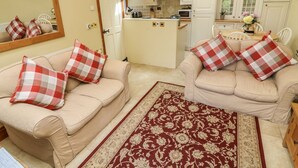 A cozy living room with two beige sofas, each adorned with red and white checkered pillows, and a large red and beige patterned rug. - Courtyard Cottage (Kendal)