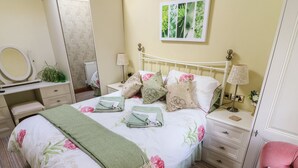 A neatly arranged bedroom with a bed, bedside tables, a chair, and a mirror. - Courtyard Cottage (Kendal)