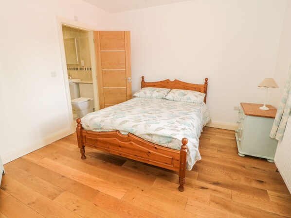 A bedroom with a wooden bed, a nightstand, a lamp, and an open bathroom door. - Hen Stabl (Beaumaris)