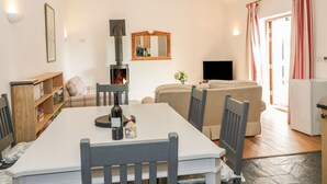 Una sala de estar acogedora con chimenea, una mesa de comedor con sillas, un sofá, un televisor y una cocina visible a través de una puerta abierta.