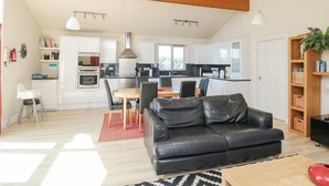 A modern living room with a black leather sofa, a dining table with chairs, and a kitchen in the background. - Orchard Lodge (Morpeth)