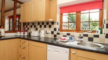 A kitchen with wooden cabinets, a black countertop, a dishwasher, and a window with a red blind.