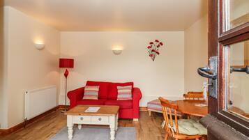 Un salon chaleureux avec un canapé rouge, une table basse en bois, une table à manger avec des chaises, un radiateur et un luminaire fixé au mur.
