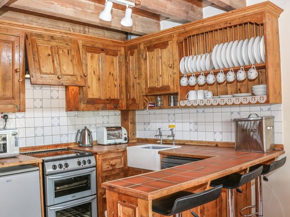 Una cocina con armarios de madera, salpicadero de azulejos, estufa, lavaplatos y un recipiente para pan.
