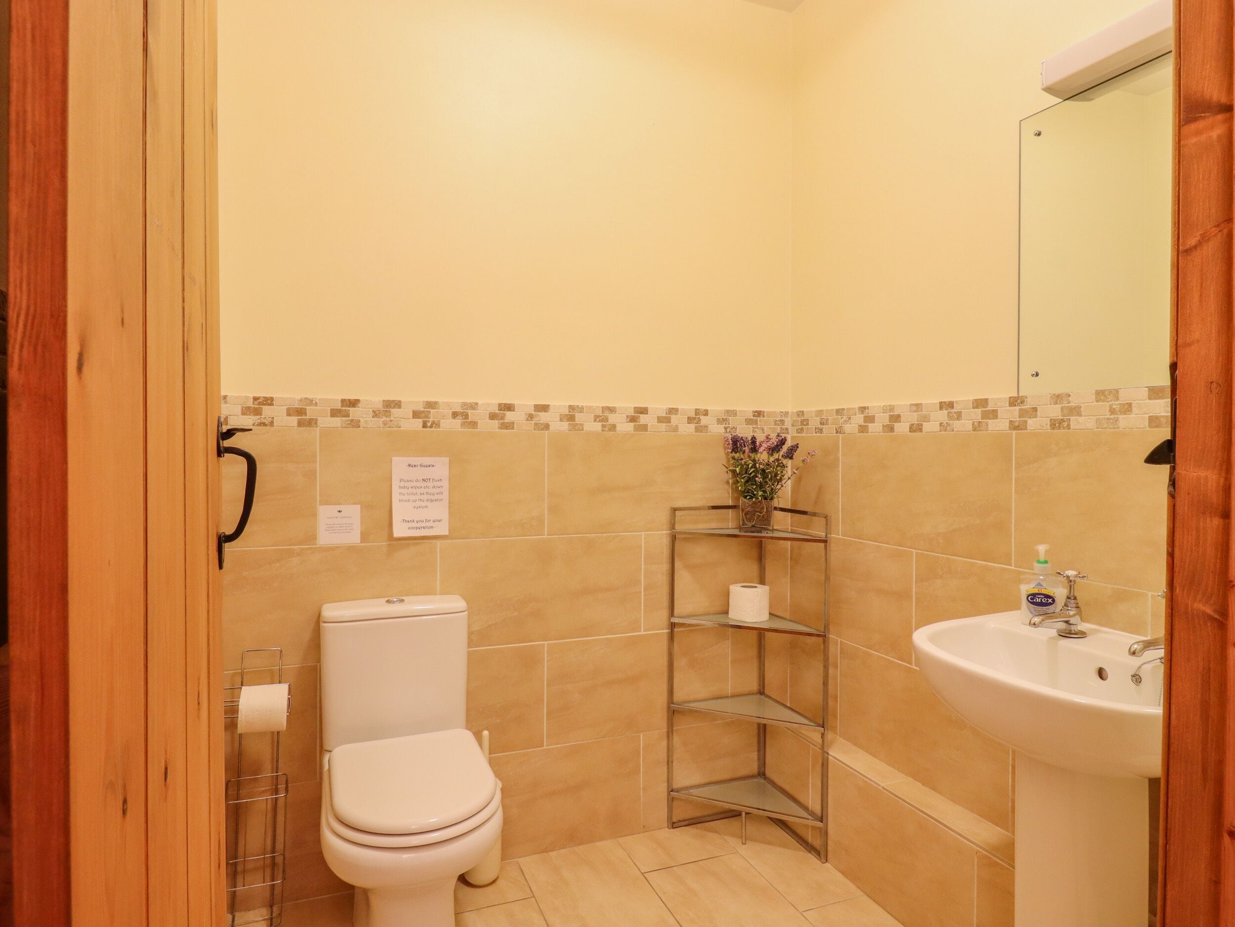 A bathroom with a toilet, a sink, a mirror, and a shelf with a vase.