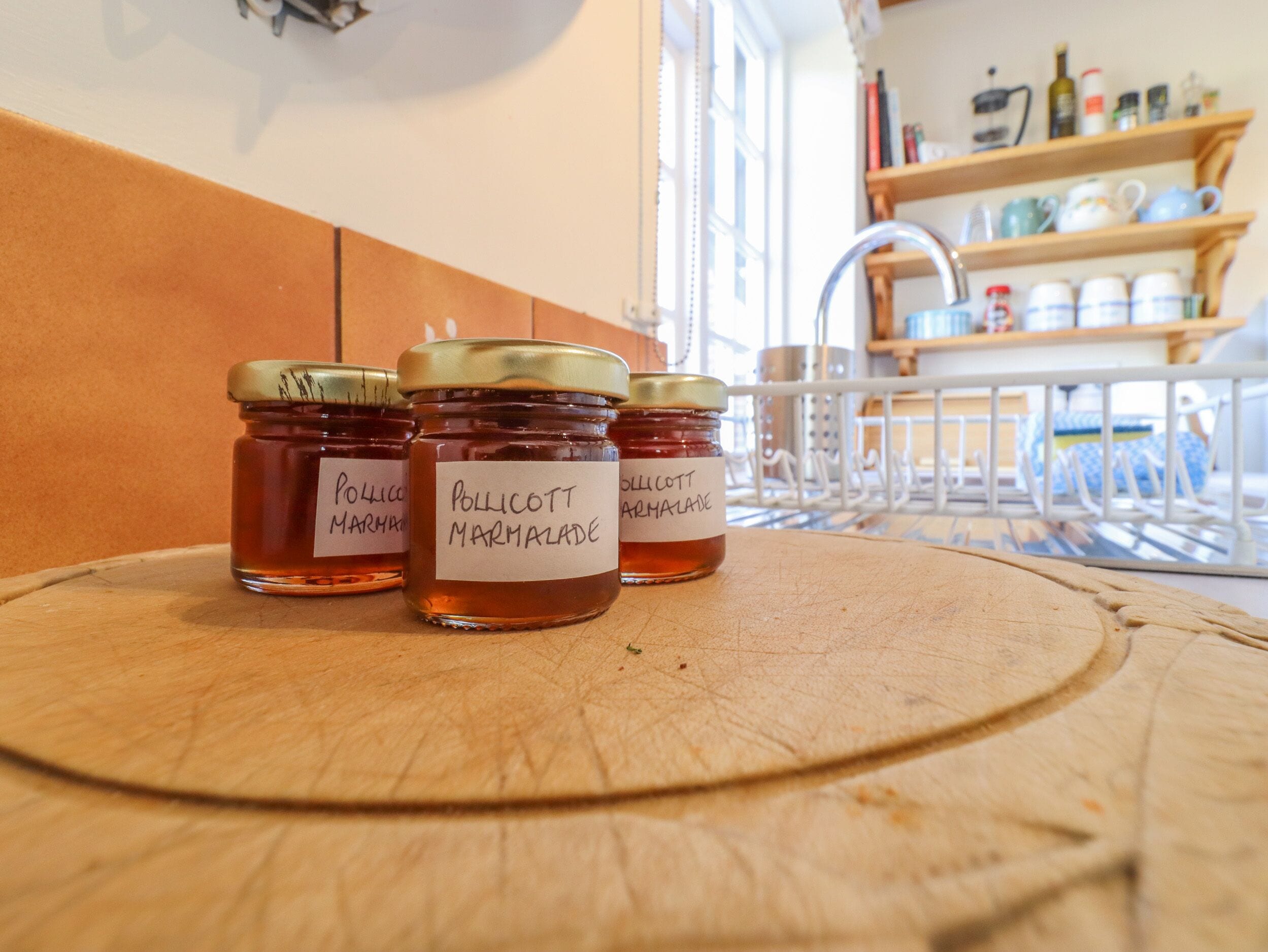 Tres botes de mermelada Pollicott sobre una superficie de madera con un fondo de cocina.