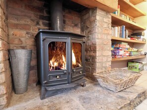 A wood-burning stove with visible flames, a metal bucket, and a wicker basket on a stone floor. - The Lodge (Scarborough)