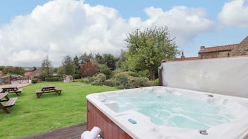 A hot tub in a backyard with picnic tables and a grassy lawn.