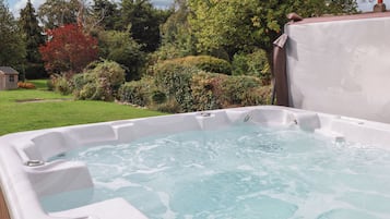 A hot tub in a garden with a grassy lawn and trees.