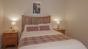Una cama bien hecha con una manta escocesa, dos mesitas de noche con lámparas, un cabecero de madera y una obra de arte enmarcada sobre la cama.