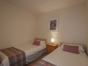 A small, simple room with two single beds, a nightstand with a lamp, and a framed picture on the wall.