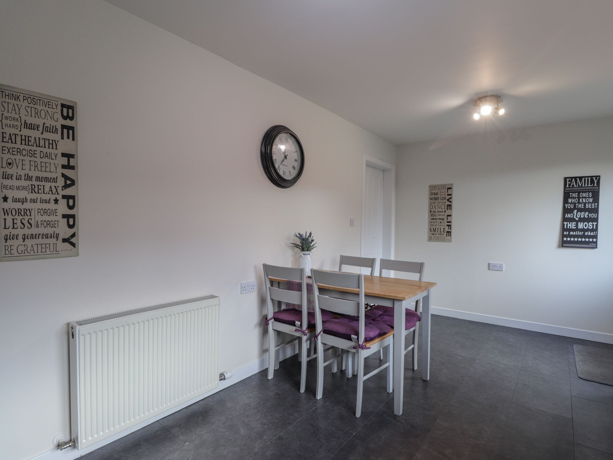 A dining area with a table and chairs, a wall clock, and motivational posters.