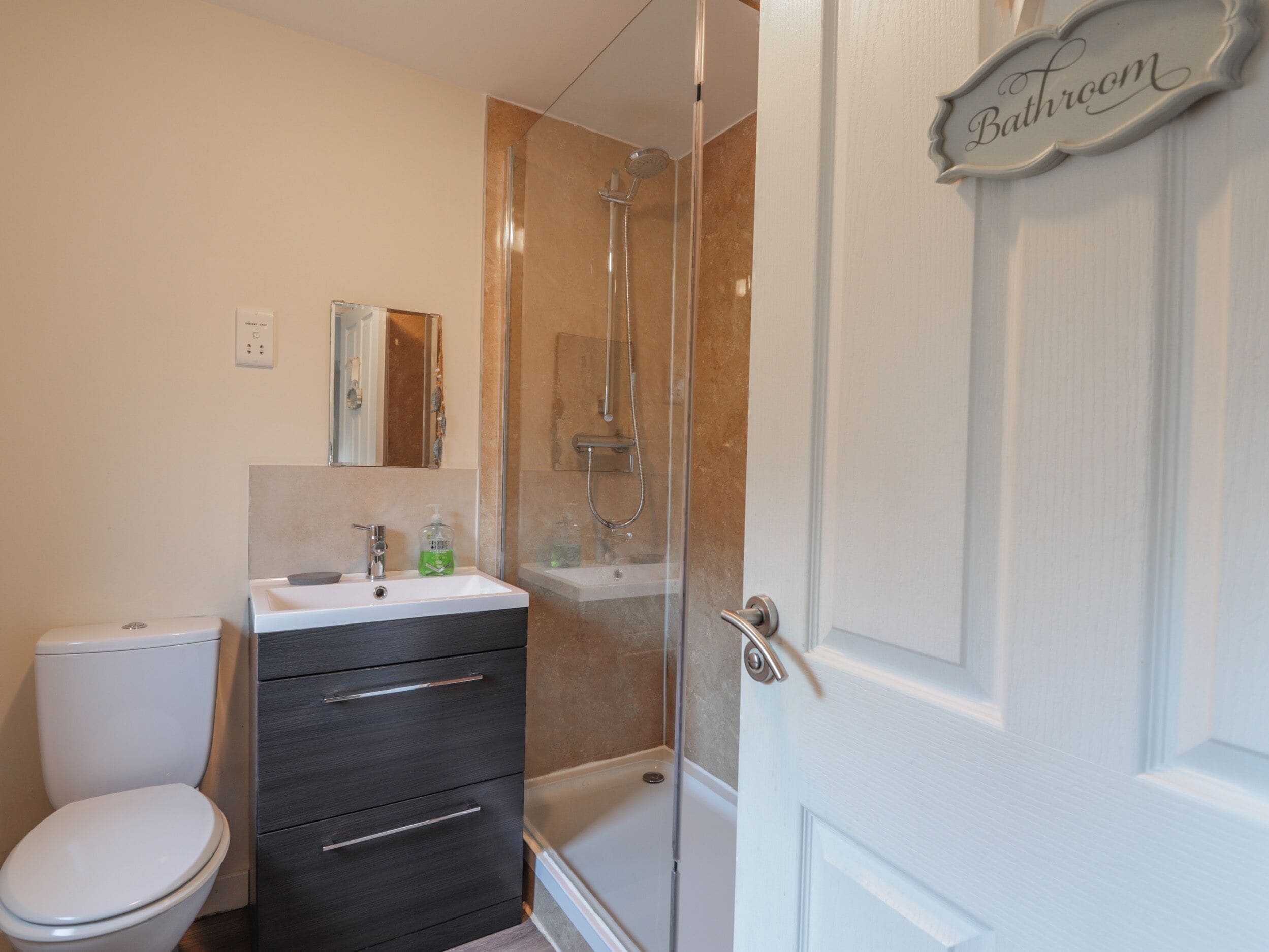 A bathroom with a toilet, sink, mirror, and shower.
