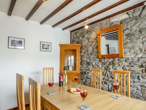 Un comedor con una mesa de madera, sillas y una pared de piedra. Hay cuadros en la pared y un espejo sobre la mesa.