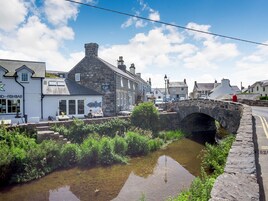 Un puente de piedra sobre un pequeño arroyo, con edificios a ambos lados, incluyendo un café y un bar de pescado.