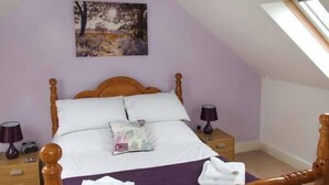 Un dormitorio con una cama con dosel de madera, dos mesitas de noche, un buró y una manta morada, además de un cuadro en la pared.