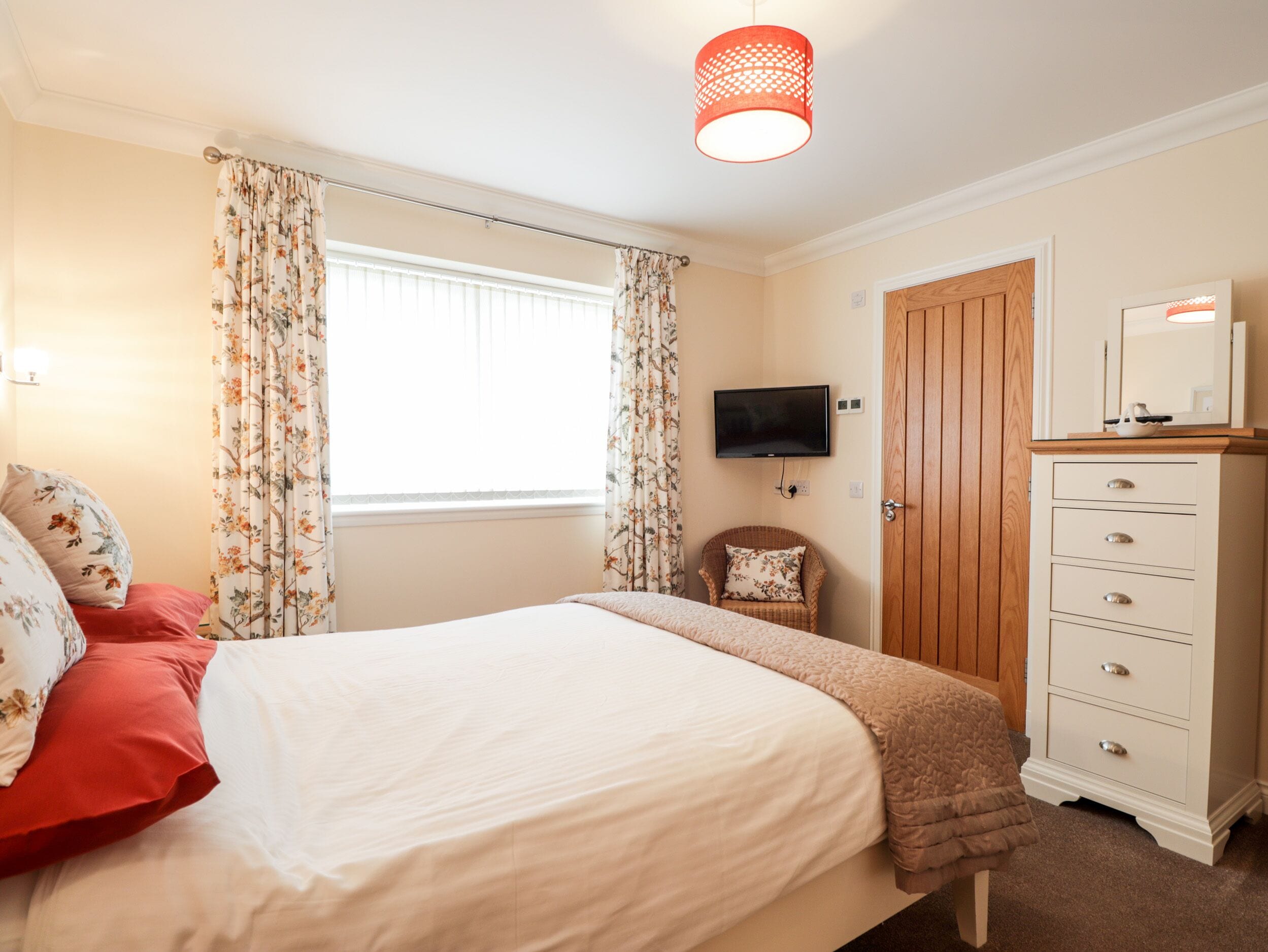 A bedroom with a bed, a dresser, a television, and a chair.