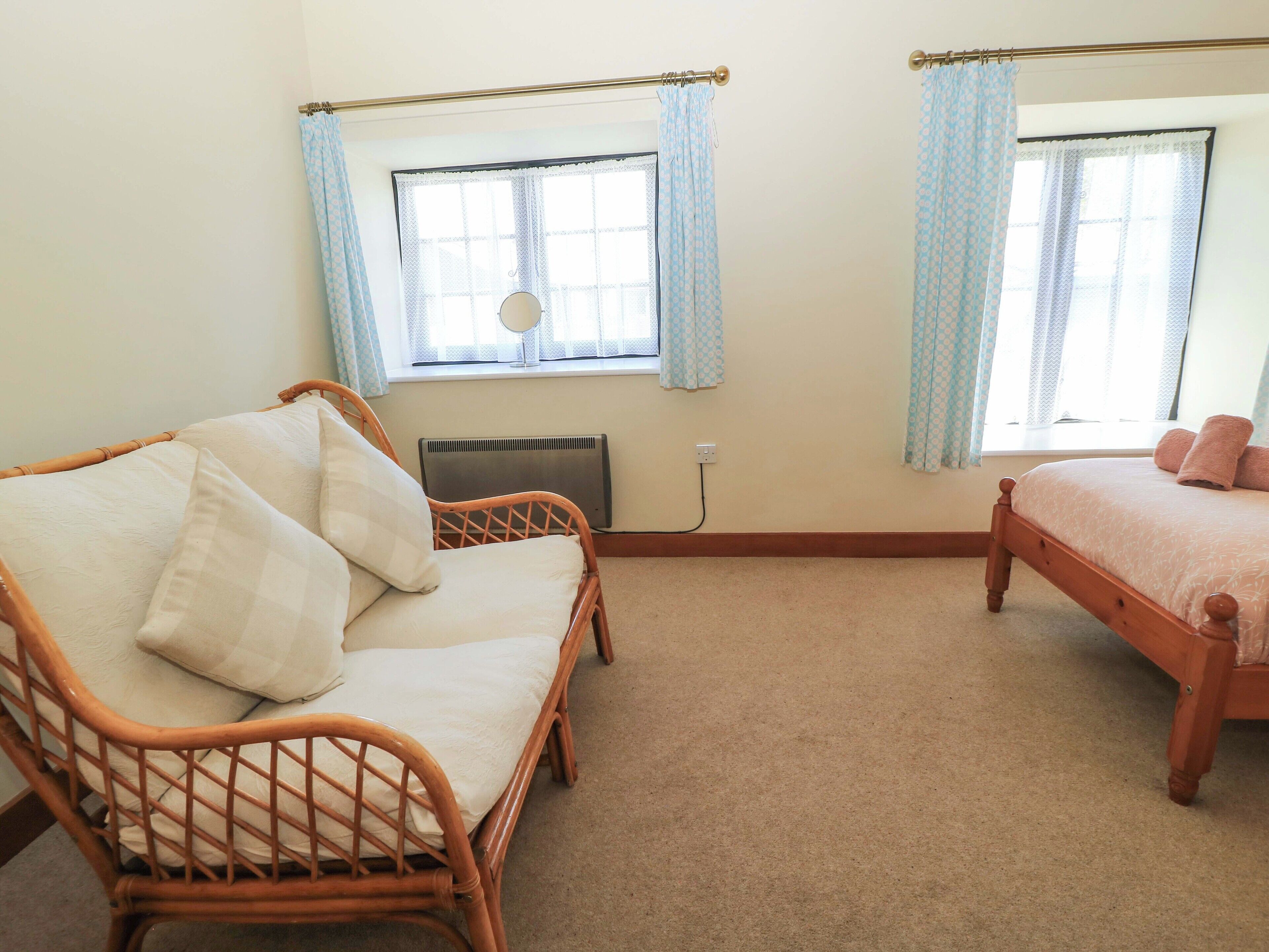 Quarto com duas camas de madeira, um sofá de vime e um radiador.
