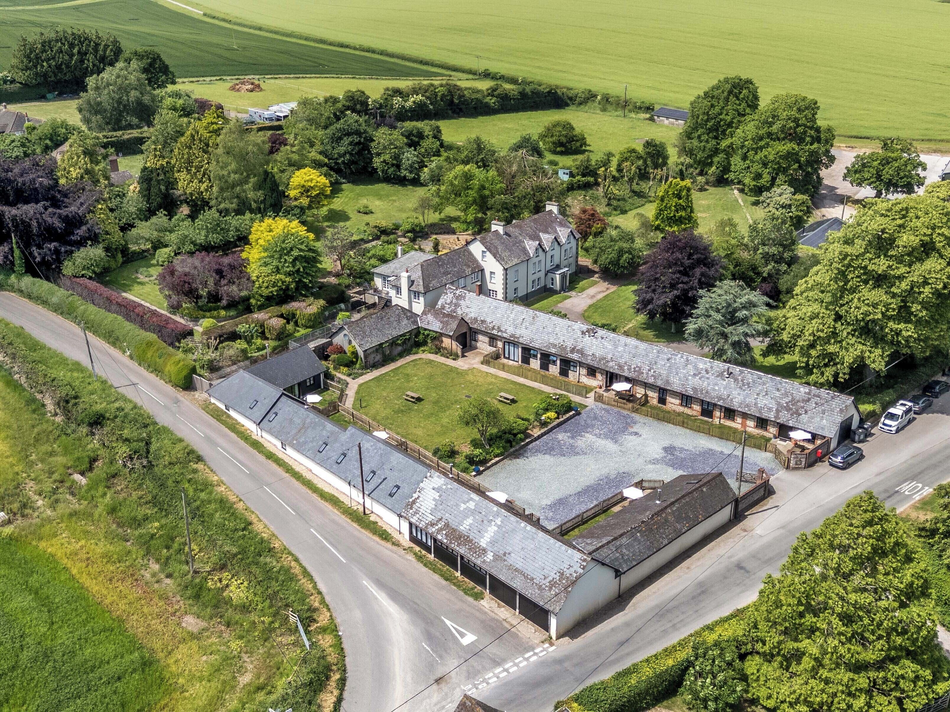 Ett flygbildsbild av en stor, historisk byggnad med flera flyglar, omgiven av frodig grönska och en välskött gräsmatta.