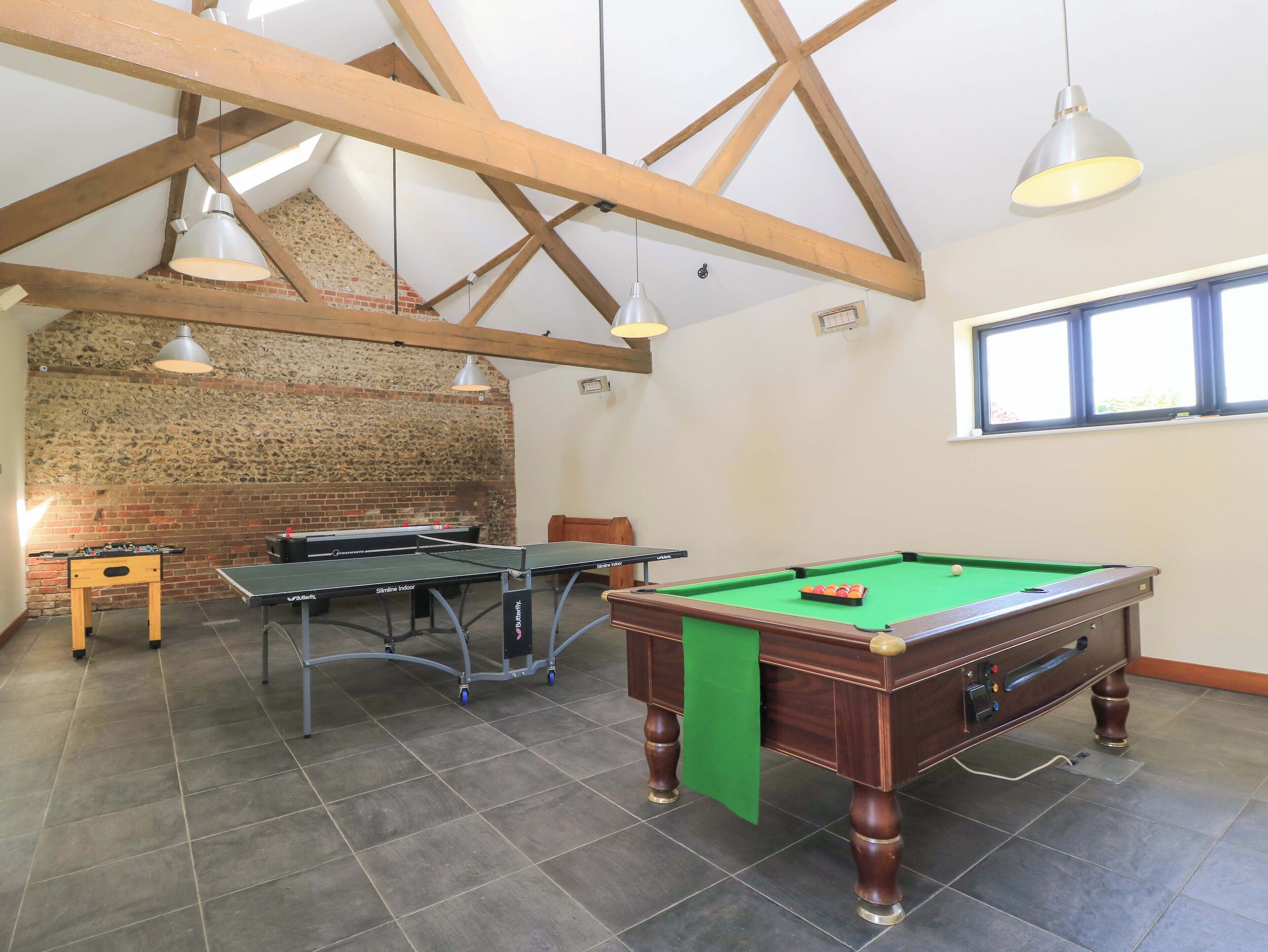 Une pièce dotée d’une table de billard, d’une table de ping-pong et d’un baby-foot, avec des poutres apparentes et un mur en briques.