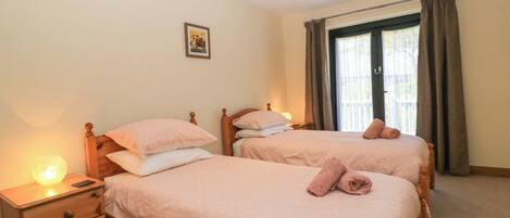Un dormitorio con dos camas individuales, una mesita de noche con lámpara, un aparador y una ventana con cortinas.