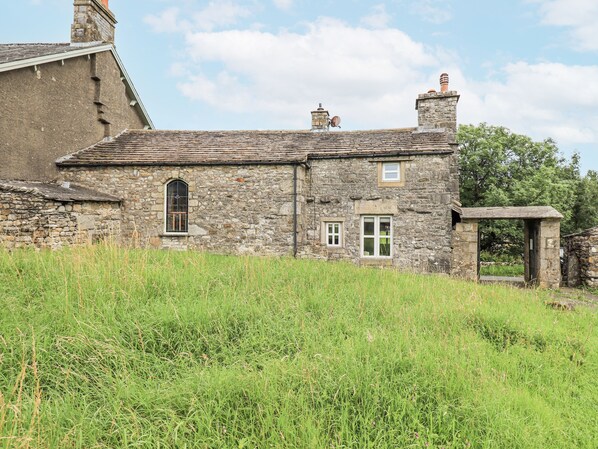 A stone building with a sloped roof, a small window, and a door. - The Stables (Settle)