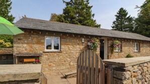 A stone cottage with a wooden gate, a welcome sign, and flower boxes.