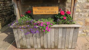 A wooden sign with "Welcome to Stable Cottage" written on it, surrounded by flower planters.