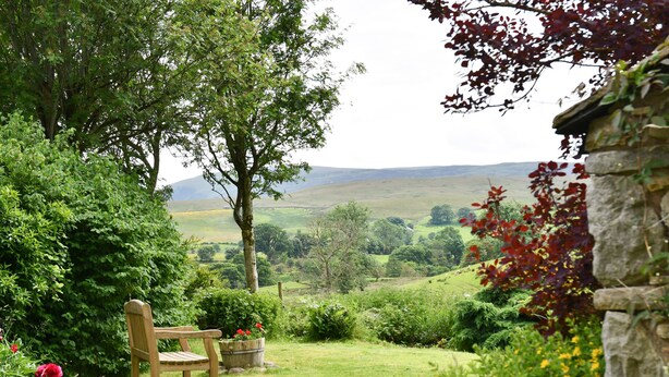 Un jardin avec une chaise en bois, un mur de pierre et une vue sur une vallée.